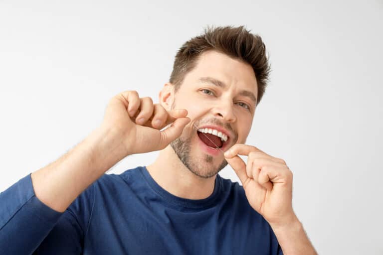 Man flossing teeth on light background