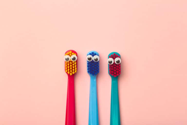 Kids toothbrushes of different colors on a pink background